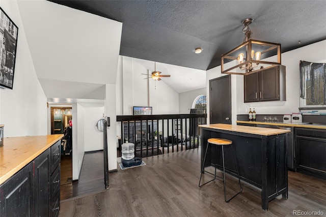 kitchen with a textured ceiling, hanging light fixtures, a kitchen island, lofted ceiling, and wood counters