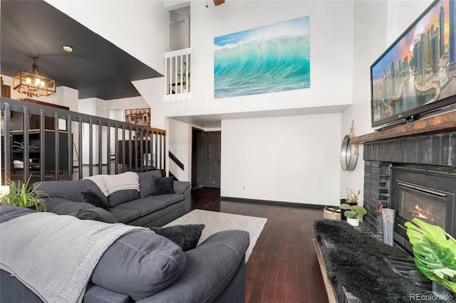 living room with a towering ceiling, dark hardwood / wood-style flooring, a brick fireplace, and a notable chandelier