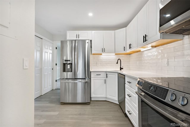 kitchen with appliances with stainless steel finishes, white cabinetry, light hardwood / wood-style floors, sink, and backsplash