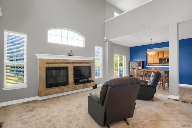 living area with a tiled fireplace, a towering ceiling, light tile patterned flooring, and baseboards