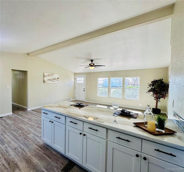 kitchen with wood-type flooring, vaulted ceiling with beams, a textured ceiling, and light stone counters