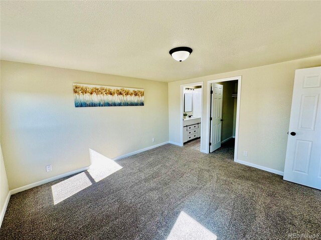 unfurnished bedroom featuring a closet, a textured ceiling, carpet, a walk in closet, and ensuite bathroom