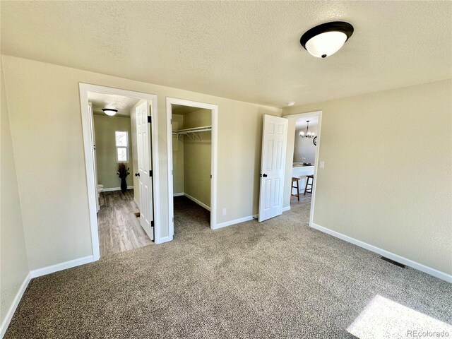 unfurnished bedroom featuring light colored carpet, a textured ceiling, a closet, and a spacious closet