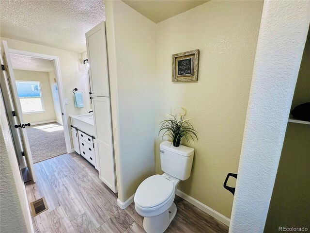 bathroom with wood-type flooring, a textured ceiling, vanity, and toilet