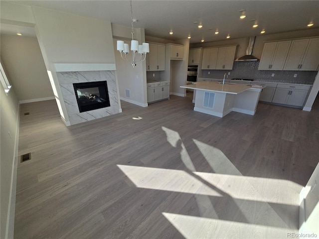 kitchen with tasteful backsplash, wall chimney exhaust hood, a fireplace, hardwood / wood-style floors, and an island with sink