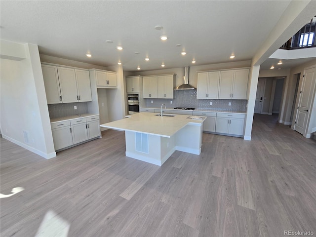 kitchen with white cabinetry, sink, wall chimney exhaust hood, an island with sink, and light hardwood / wood-style floors