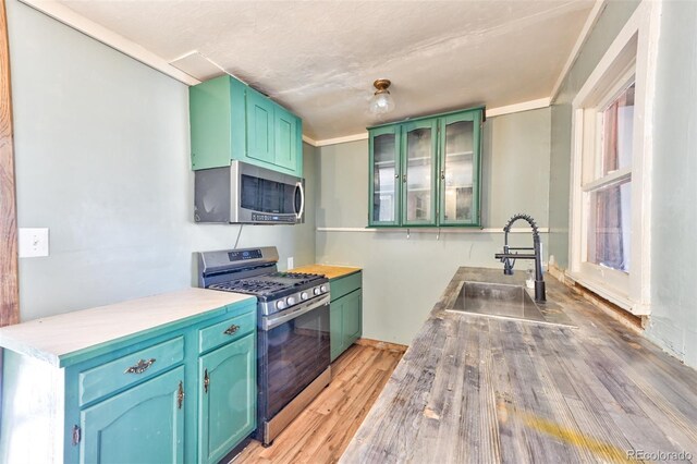 kitchen with stainless steel appliances, crown molding, sink, green cabinetry, and light hardwood / wood-style floors