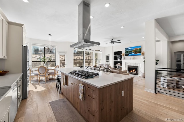 kitchen with stainless steel gas stovetop, light wood-type flooring, a fireplace, and island range hood