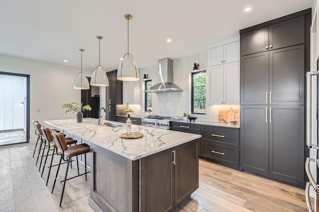 3019 Chase St, Wheat Ridge, CO 80214 - kitchen featuring wall chimney range hood, a sink, stainless steel range oven, a kitchen island with sink, and a breakfast bar area