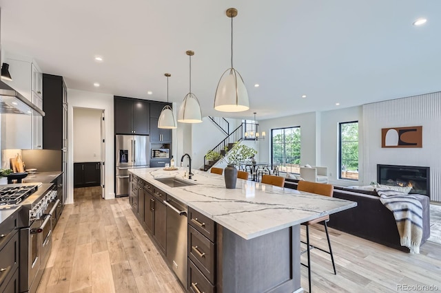 3019 Chase St, Wheat Ridge, CO 80214 - kitchen with stainless steel appliances, a sink, a breakfast bar, light wood finished floors, and a kitchen island with sink