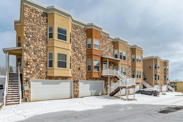 snow covered property with a garage and stairs