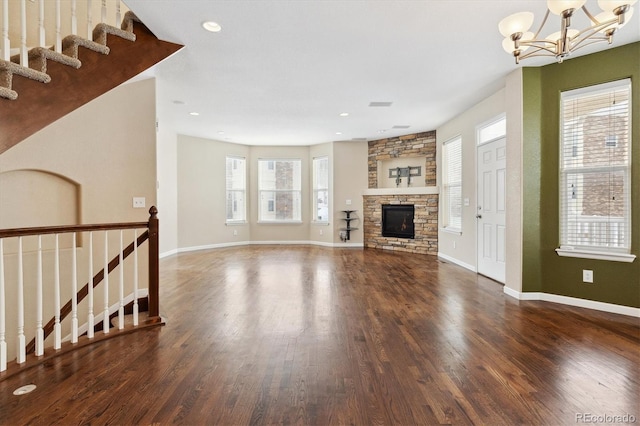 unfurnished living room featuring a notable chandelier, baseboards, wood finished floors, and a stone fireplace