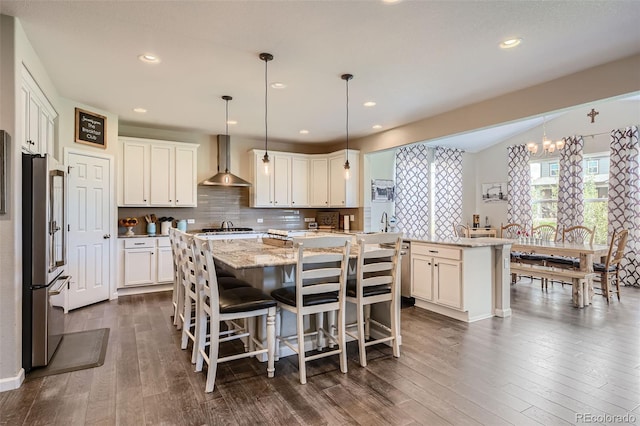 kitchen featuring stainless steel appliances, decorative backsplash, dark wood-type flooring, a kitchen island, and wall chimney range hood