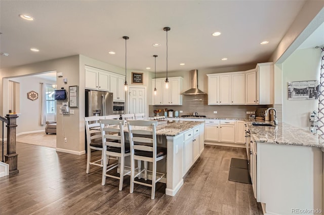 kitchen with tasteful backsplash, wall chimney exhaust hood, appliances with stainless steel finishes, dark wood-type flooring, and a sink