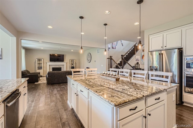 kitchen featuring a fireplace, stainless steel appliances, recessed lighting, dark wood-type flooring, and light stone countertops