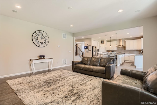 living room featuring stairs, dark wood-type flooring, visible vents, and baseboards