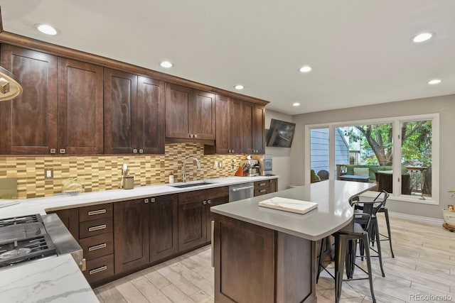 kitchen with tasteful backsplash, dark brown cabinetry, sink, light hardwood / wood-style floors, and a breakfast bar area