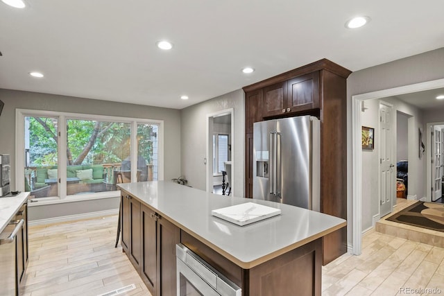 kitchen with dark brown cabinetry, a kitchen island, light wood-type flooring, and appliances with stainless steel finishes