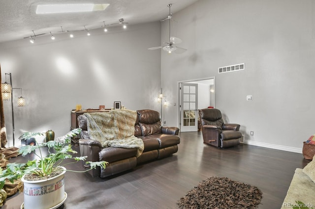 living room with a towering ceiling, a textured ceiling, dark hardwood / wood-style flooring, and ceiling fan