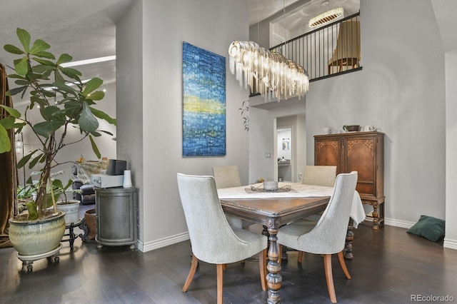 dining space with dark hardwood / wood-style flooring, a towering ceiling, and an inviting chandelier