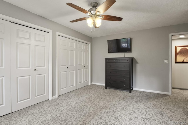 unfurnished bedroom with a textured ceiling, light colored carpet, ceiling fan, and multiple closets