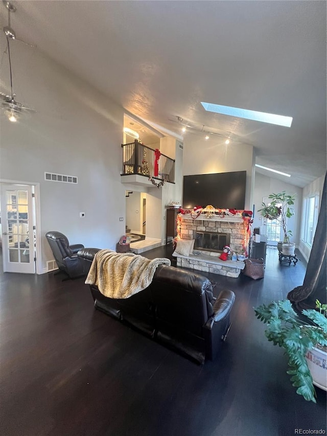 living room with ceiling fan, a stone fireplace, wood-type flooring, and a skylight