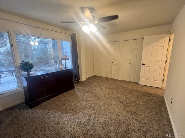 carpeted bedroom with multiple windows, ceiling fan, two closets, and a textured ceiling