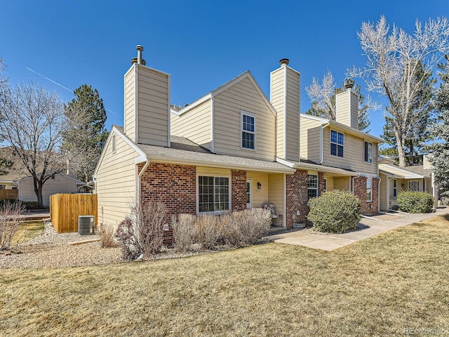 view of front of home featuring central air condition unit, brick siding, fence, a chimney, and a front yard