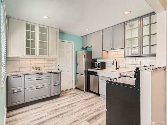 kitchen with glass insert cabinets, stainless steel appliances, gray cabinetry, light wood-type flooring, and a sink