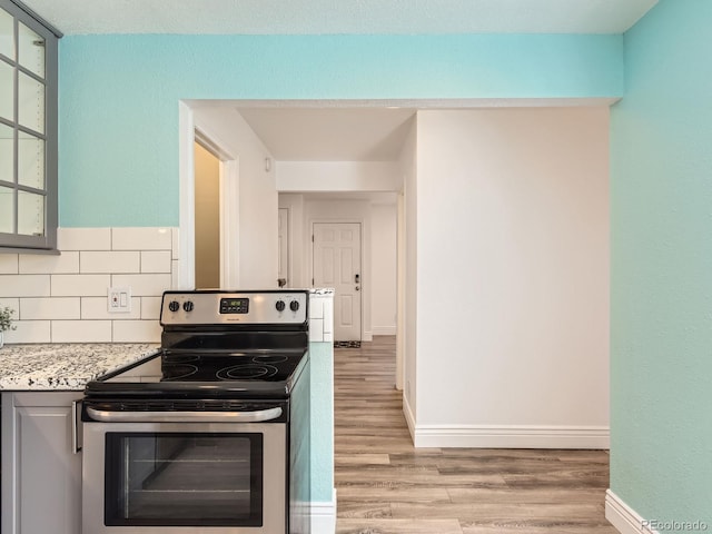 kitchen with baseboards, decorative backsplash, electric stove, light wood-style flooring, and glass insert cabinets