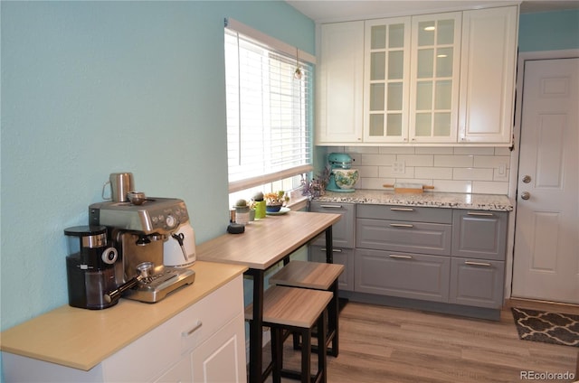 kitchen featuring decorative backsplash, glass insert cabinets, gray cabinets, light countertops, and light wood-type flooring