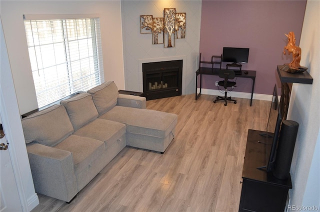 living room featuring a fireplace, light wood-style flooring, and baseboards