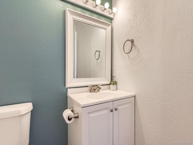 half bathroom featuring toilet, vanity, and a textured wall