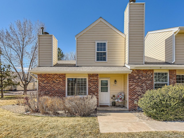 traditional-style house featuring roof with shingles, brick siding, a chimney, and a front yard