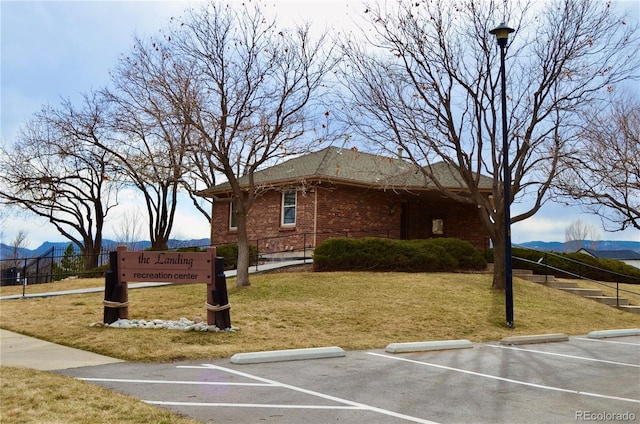 view of home's exterior with brick siding, uncovered parking, a lawn, fence, and a mountain view