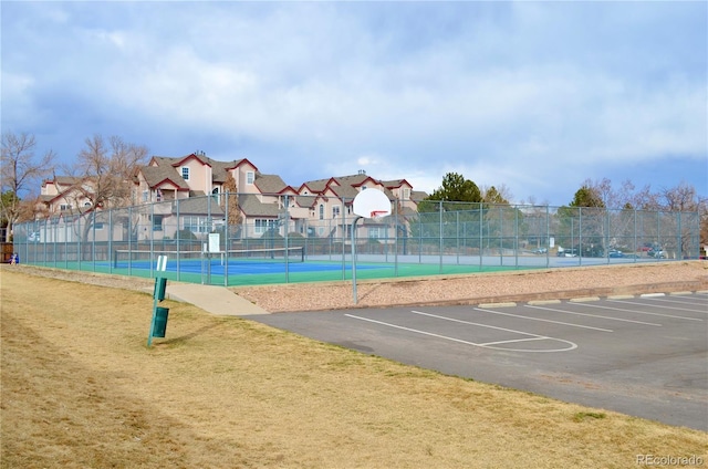 exterior space with a tennis court, a lawn, community basketball court, fence, and a residential view