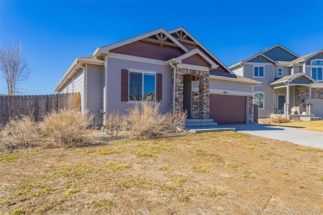 view of front of property with stone siding, an attached garage, concrete driveway, and fence