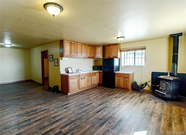 kitchen featuring dark wood-type flooring, a wood stove, sink, and black refrigerator