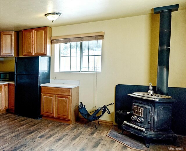 kitchen featuring hardwood / wood-style flooring, a wood stove, and black refrigerator