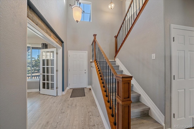 entryway featuring stairs, a towering ceiling, light wood-style flooring, and baseboards