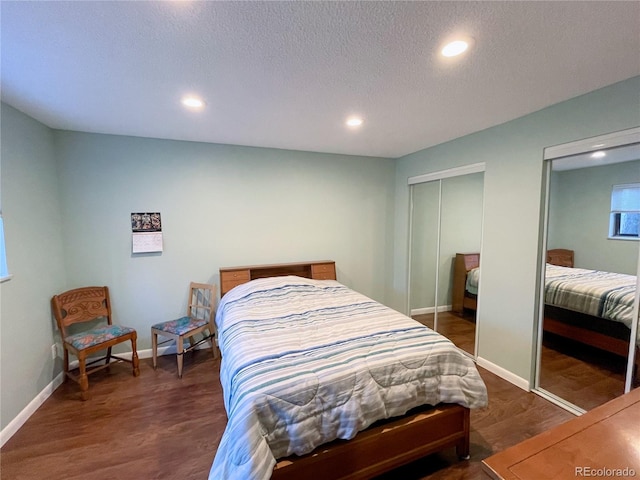 bedroom with two closets, dark hardwood / wood-style flooring, and a textured ceiling