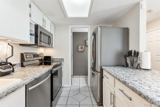 kitchen featuring appliances with stainless steel finishes, light tile patterned flooring, light stone counters, and white cabinets