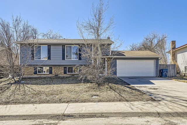 split level home featuring concrete driveway, brick siding, fence, and an attached garage