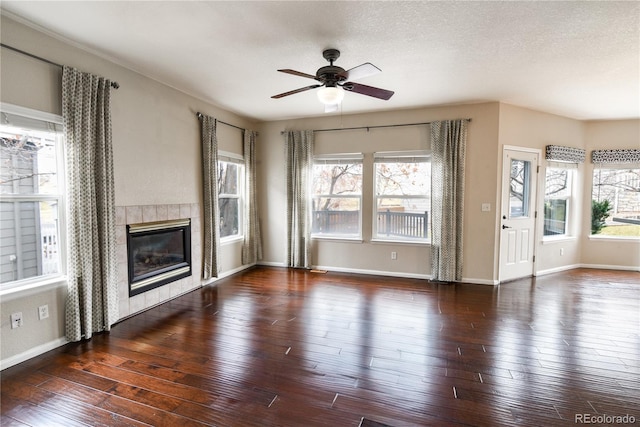 unfurnished living room featuring a tile fireplace, ceiling fan, dark wood-type flooring, and a textured ceiling