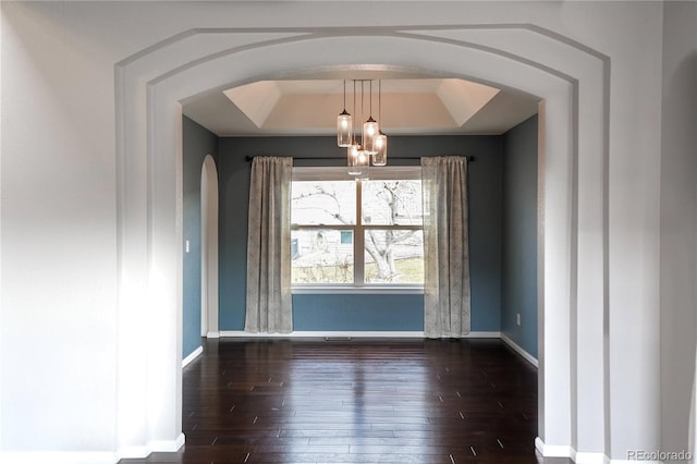 spare room with dark hardwood / wood-style flooring, a tray ceiling, and a notable chandelier