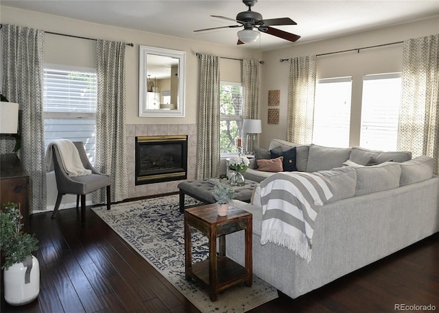 living room featuring dark hardwood / wood-style flooring, ceiling fan, a healthy amount of sunlight, and a tiled fireplace