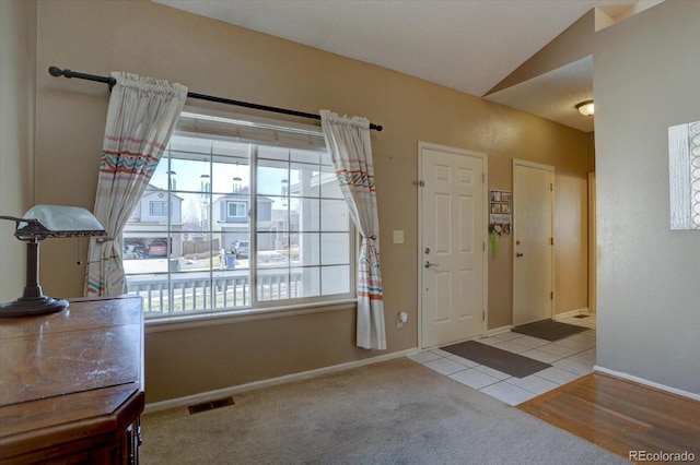 foyer entrance with tile patterned floors, visible vents, carpet, baseboards, and vaulted ceiling