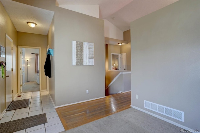 hallway with visible vents, baseboards, carpet, vaulted ceiling, and tile patterned floors