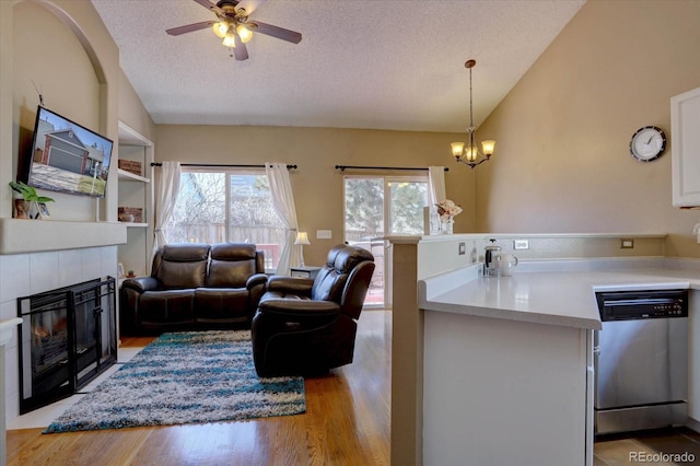 kitchen featuring a tiled fireplace, dishwasher, light wood-style floors, and lofted ceiling