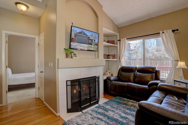 living area with a fireplace, a textured ceiling, built in shelves, and vaulted ceiling